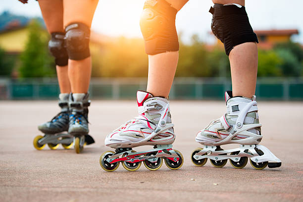 Skaters' legs protected by knee pads, wearing white and blue inline skates outdoors.