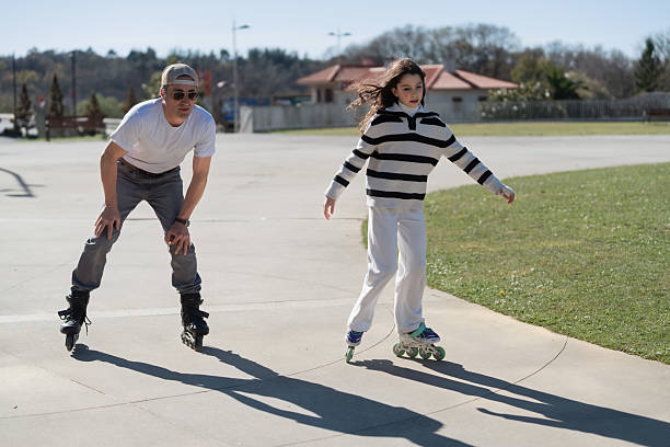 Man and girl on inline skates practicing in a sunny outdoor park.